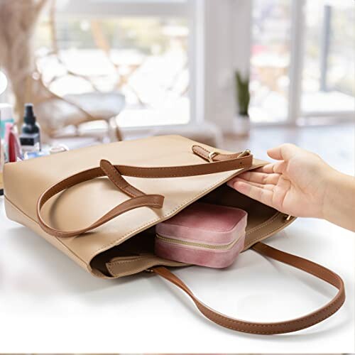 A hand reaching into an open beige tote bag with a pink pouch inside.